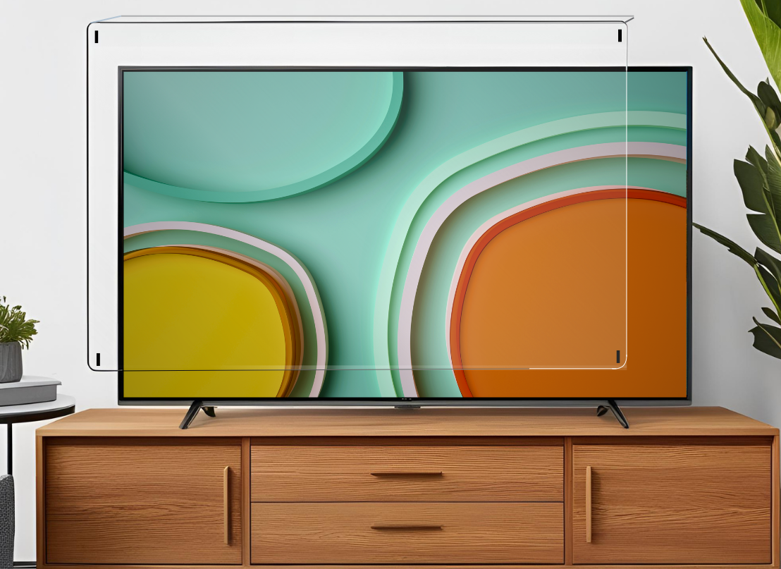 A clear, rectangular TV screen protector is shown slightly detached from a flat-screen television, illustrating its size and how it would cover the display. The TV is on a wooden cabinet and displays a colourful abstract image with teal, yellow, orange, and pink curved shapes. Small black tabs are visible at the top corners of the screen protector, likely indicating an attachment method. A blurred interior setting with plants and furniture is in the background.