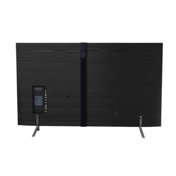 The back of a 65" Smart 4K TV is shown with a wide black strap wrapped vertically around it, suggesting how a TV screen protector might be secured. The TV is standing on its two silver, V-shaped legs. The connection ports are visible on the left side of the back panel. The background is plain white.