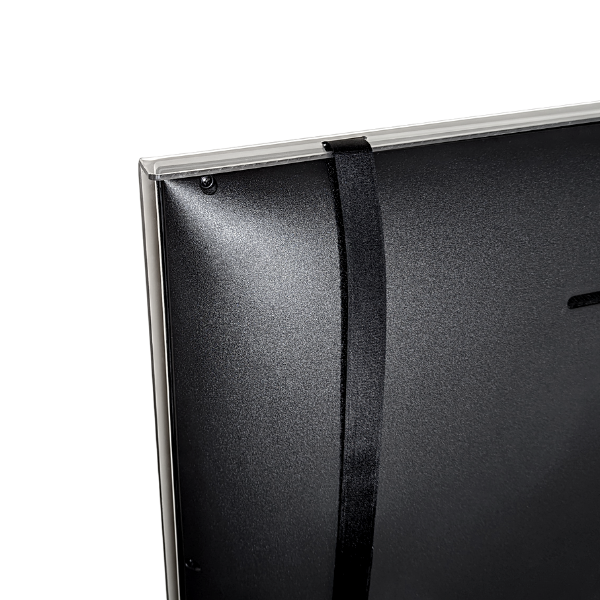 A close-up shot from the back shows a clear acrylic TV screen protector being secured to a flat-screen television with a wide black Velcro strap. The strap wraps vertically around the back of the TV, attaching to the top edge of the protector. The texture of the back of the black TV is visible. The background is plain white.