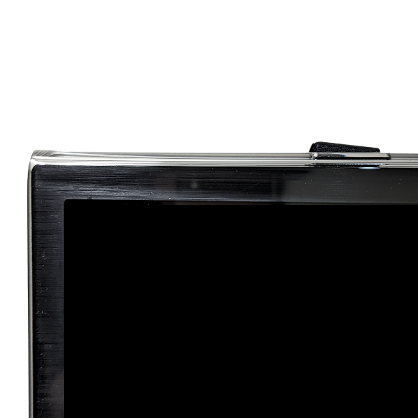 A close-up view shows the top edge of a flat-screen television with a clear acrylic screen protector partially installed. A black Velcro strap is visible at the top, securing the protector to the back of the TV. The protector slightly extends beyond the top and side edges of the black TV screen. The background is pure white.