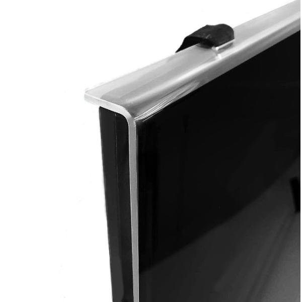 A close-up shot shows the top corner of a clear acrylic TV screen protector being held in place by a black Velcro strap that wraps around the back of a flat-screen television. The protector slightly overhangs the edge of the black TV screen. The background is plain white.