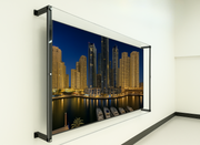 A clear, protective TV enclosure is mounted on a white wall, showcasing a vibrant image of a city skyline at night with lights reflecting on the water and several boats docked. The enclosure appears sturdy and well-fitted.
